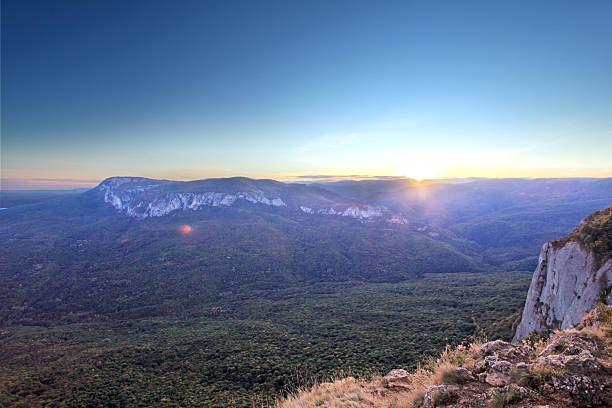 Majestic mountain ridge stretching above a dense forest with steep rocky cliffs and soft light illuminating the peaks.