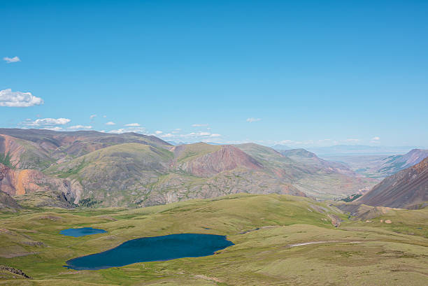 Two beautiful blue lake among green hills in sunlight. Sunlit valley between multicolor mountains in sunny day. Alpine scenery of many pastel colors in bright sun. Mountain range silhouette far away.