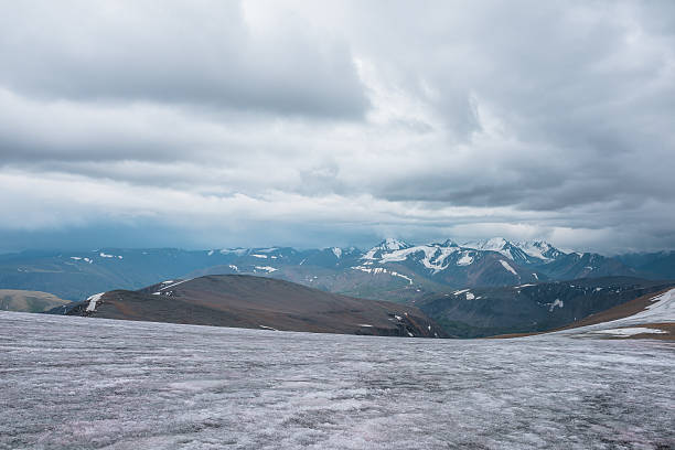 istock Dramatic panoramic view from big glacier to wide alpine valley and large snow-capped mountain range in rainy low clouds. Awesome vast landscape with high snowy mountains in rain under gray cloudy sky. 2241932629