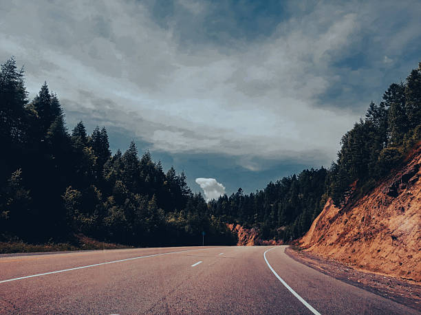 A view from a car on a small country road, surrounded by forests and mountain cliffs on either side. Cinematic black depth effect.