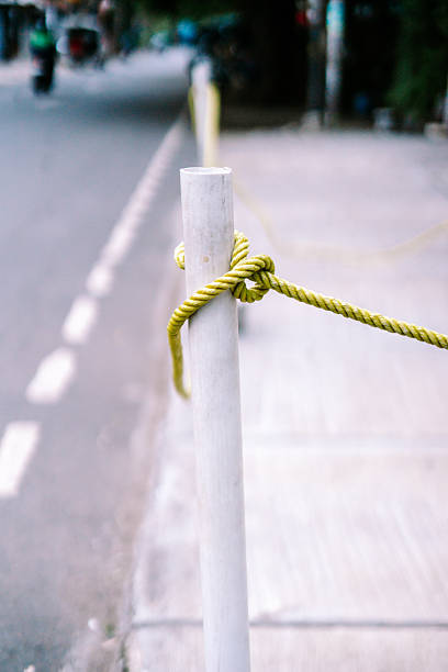 A bright yellow-green rope tightly tied with a knot around a white pole, set against a softly blurred urban street scene with a sidewalk and road in daylight.