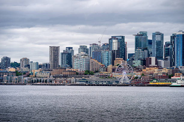 A dramatic view of downtown Seattle, Washington, captured from across Puget Sound under heavy clouds. The modern skyline features iconic skyscrapers and waterfront buildings, illustrating the city’s urban density and architectural diversity.