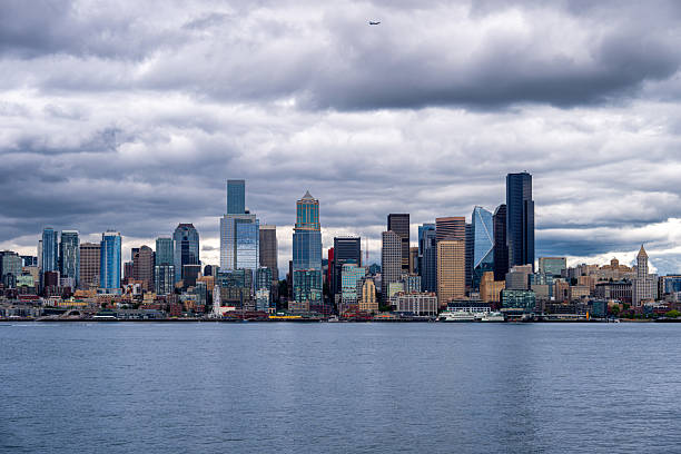 A dramatic view of downtown Seattle, Washington, captured from across Puget Sound under heavy clouds. The modern skyline features iconic skyscrapers and waterfront buildings, illustrating the city’s urban density and architectural diversity.