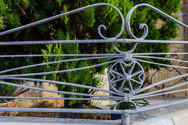 A decorative wrought iron gate features curved scrollwork and a star-shaped medallion set against vibrant green shrubs. This imperial-style detail highlights garden architecture, metalwork, and ornamental fencing.