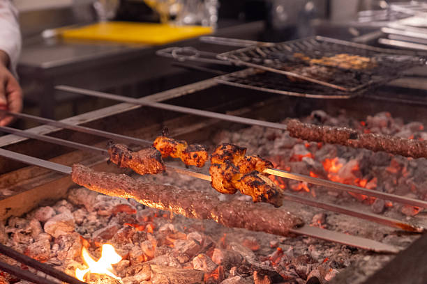 Close-up of juicy marinated chicken skewers being grilled over glowing charcoal embers. Traditional barbecue preparation with skewers suspended above the fire, capturing the heat, smoke, and rustic cooking atmosphere. Perfect for illustrating concepts of outdoor grilling, street food, or authentic culinary traditions.