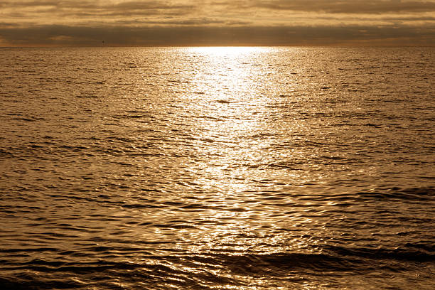 The sun is setting over the ocean, casting a warm glow on the water. The sky is filled with clouds, creating a serene and peaceful atmosphere