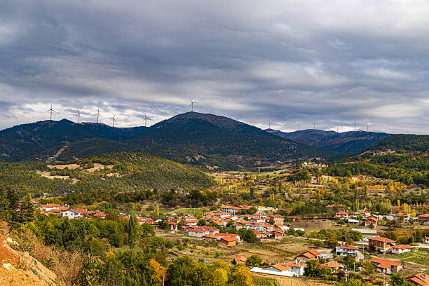 Scenic rural village surrounded by green hills and mountain landscape covered with lush green and yellow autumn trees.
