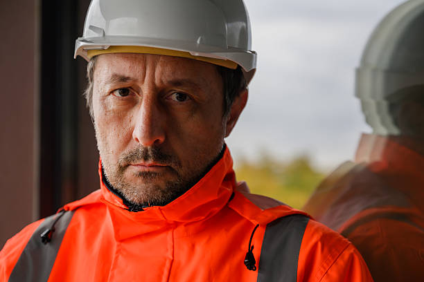 Young adult engineer wearing safety vest and hardhat inspecting construction site progress