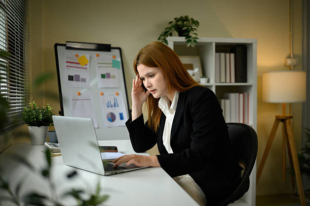 istock A Caucasian businesswoman looking stressed while working on a laptop in a modern office setting with charts and documents in the background 2241973882