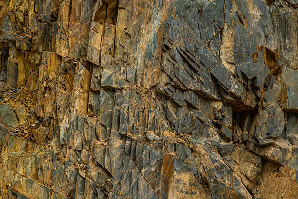 Rugged rock formation stands majestically in mountainous region during daytime. Textured surfaces and rough contours create a dramatic outdoor landscape, evoking a sense of solitude and strength.