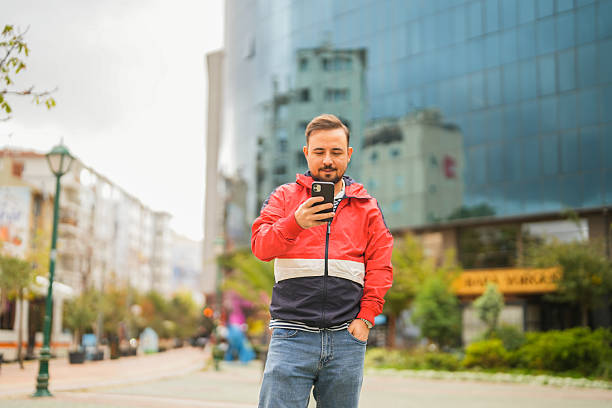 Man standing outdoors in the city using smartphone with modern glass building background