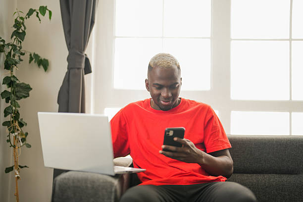 istock Young African man working remotely on laptop while using smartphone at home 2241979584