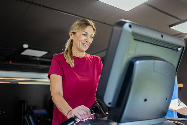 istock Mature woman smiling while exercising on treadmill in gym 2241980287