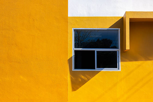 Minimalist architecture with yellow and white wall, modern window, and sunlight shadow creating geometric composition. Perfect for design and architecture concepts.