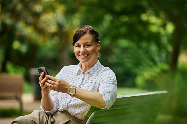 istock Smiling Woman Using Smartphone While Sitting on a Park Bench 2241982768