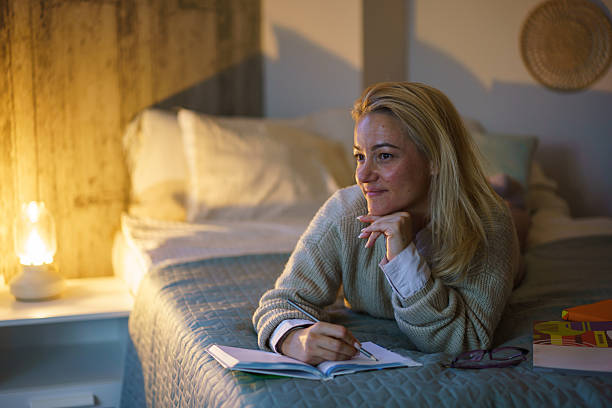 Woman is at home by herself in her apartment in the city. She is writing in her journal diary, a great way to contemplate life and mental wellbeing.