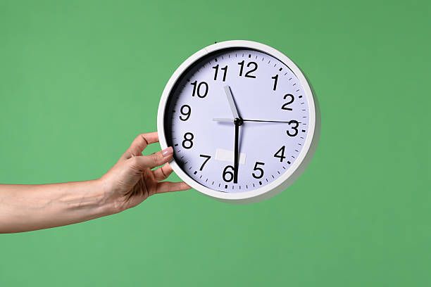 istock Woman Hand Holding Clock on Green Background 2241994187