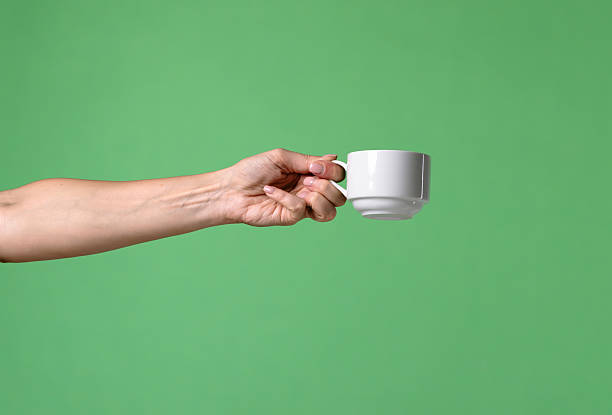 istock Woman Hand Holding White Ceramic Cup on Green Background 2241994323