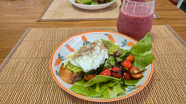 Poached egg and avocado toast with fresh salad and berry smoothie on wooden table
