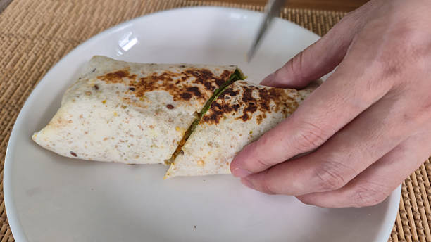 istock Hand cutting a burrito wrap on a white plate at home dining 2241995367