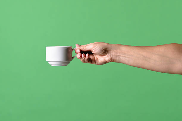 istock Woman Hand Holding White Ceramic Cup on Green Background 2241998352