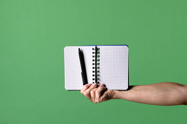 istock Woman Hand Holding Open Notebook with Pen on Green Background 2241998462