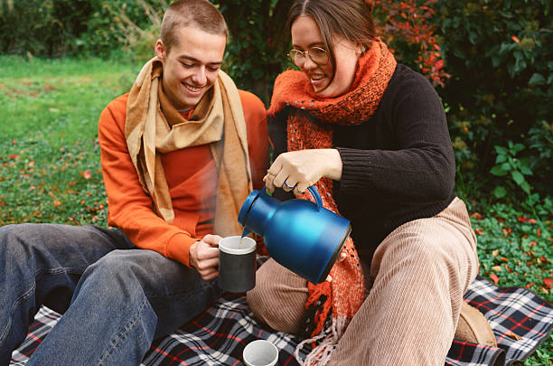 Two friends enjoy a warm drink together on a plaid blanket in a lush autumn garden. Wrapped in cozy scarves and sharing smiles, they capture the warmth of companionship and simple outdoor joy on a crisp fall afternoon. Copy space for text, high angle view - Autumn, lifestyle
