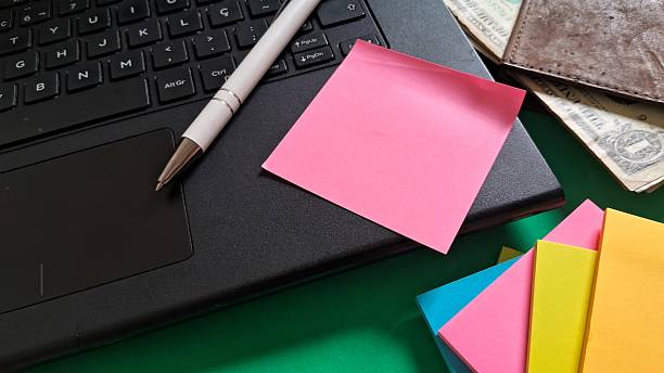 istock Desk essentials with laptop, colorful post-its, pen and leather wallet with dollars inside on green background 2242001662