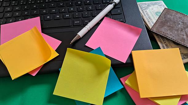 istock Desk essentials with laptop, colorful post-its, pen and leather wallet with dollars inside on green background 2242001691