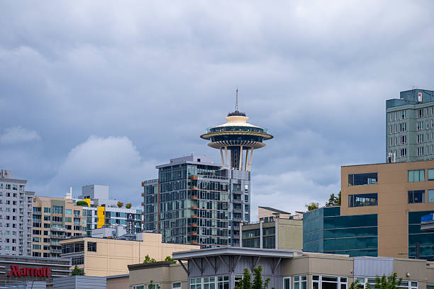 The iconic Space Needle rises behind a cluster of modern residential and commercial buildings in Seattle, Washington. Captured under a cloudy sky, the image showcases the city’s architectural blend of historic landmarks and urban development.