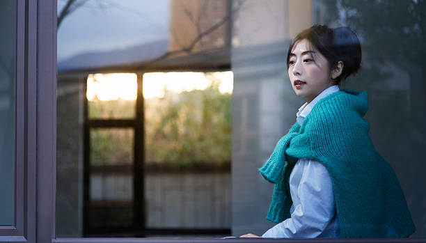 istock Beautiful young woman looking through the window at home 2242005575