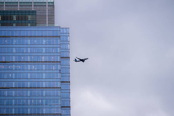 A commercial United Airlines airplane passes between two tall skyscrapers in downtown Seattle, Washington, under a cloudy sky. The dramatic urban moment captures motion, modern architecture, and aviation in a single frame.