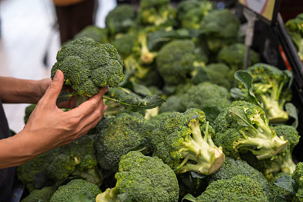 Close-up of a person selecting fresh broccoli from a supermarket display, representing healthy eating, freshness, and daily grocery shopping.