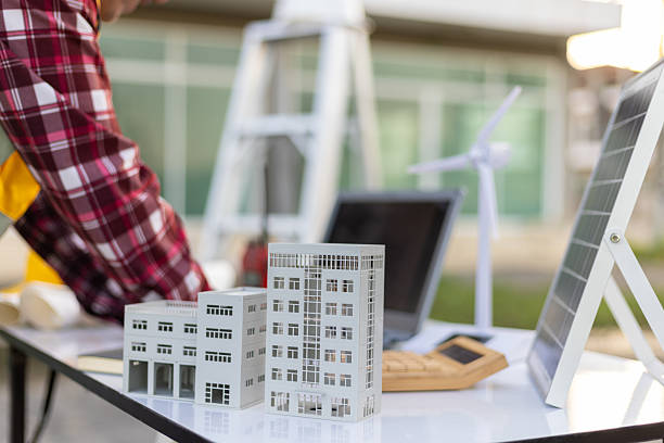 istock Contractor working on sustainable building project, evaluating scale models of buildings alongside miniature solar panel and wind turbine. 2242010224
