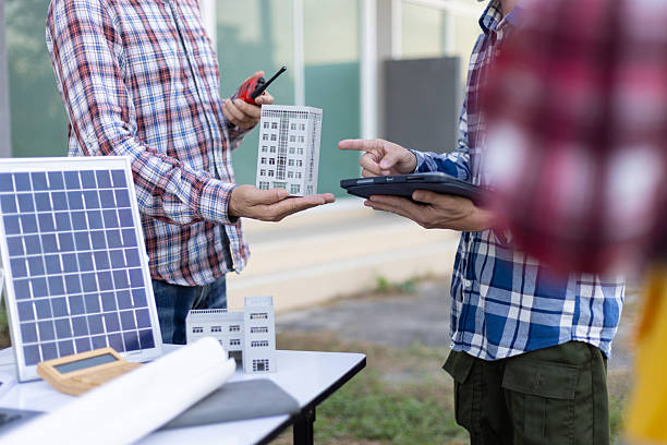 istock Contractors discussing a sustainable building project, holding a scale model of a building and a solar panel, incorporating renewable energy solutions. 2242010251