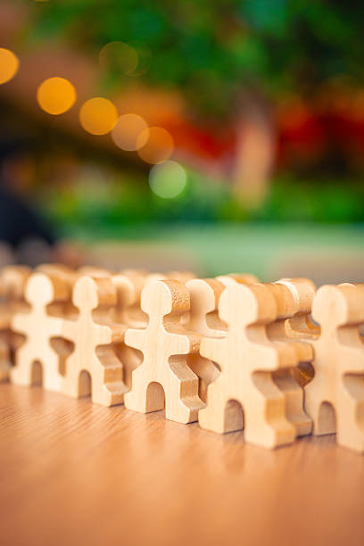 istock Wooden human figures holding hands in a row on table, with blurred colorful background. Concept for unity, teamwork, cooperation, diversity, support, togetherness, community, and collaboration. 2242010422