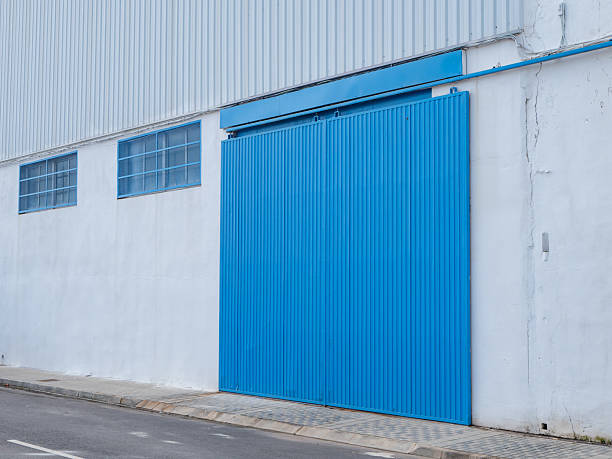 istock bright blue industrial sliding gate stands closed against plain white wall. setting is urban, with clean street paved with stones nearby. scene features good lighting 2242016298
