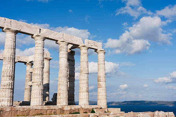 Ancient marble columns of the Temple of Poseidon stand against bright blue sky and sea horizon at Cape Sounion under warm sunlight