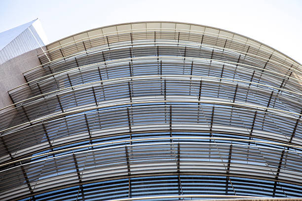 Contemporary building facade featuring a geometric pattern of gray and white panels with reflective windows under a clear blue sky.