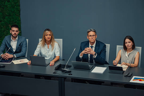 Business professionals sitting at a table, seriously following a corporate meeting or conference presentation in an office