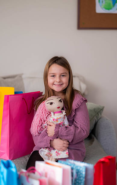 Young girl smiling, holding her new doll surrounded by colorful shopping bags and gifts