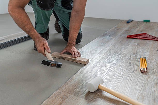 istock Floating floor work. The worker taps the board of vinyl plank to lock the click system. He is using hammer and wooden plank. 2242040913