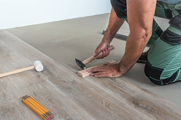 istock Floating floor work. The worker taps the board of vinyl plank to lock the click system. He is using hammer and wooden plank. 2242040915