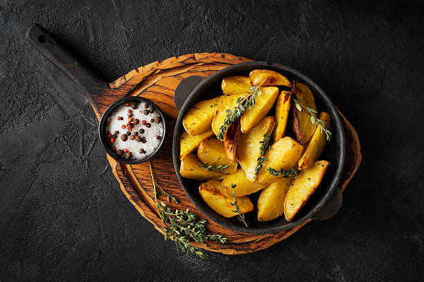 istock Roasted sliced potatoes with thyme herb, salt, peppers, cut board 2242048222