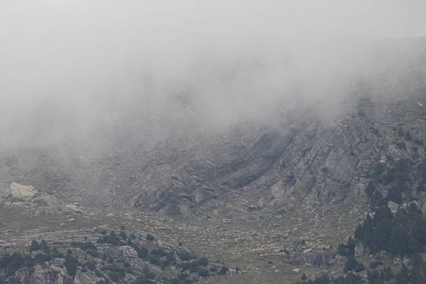 A serene mountain landscape with layers of mountains fading into the distance. The valleys between the peaks are filled with mist, creating a dreamy, ethereal effect under a soft blue sky. The scene exudes a calm and peaceful atmosphere, perfect for capturing the beauty of nature’s tranquility.