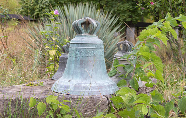 istock Old bronze church bells with decorative crowns placed outdoors surrounded by green plants and rustic wooden texture in a countryside setting 2242054996