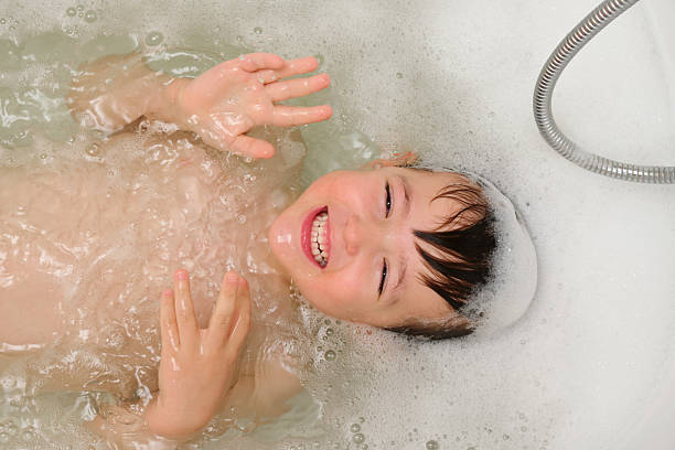istock Child making bath time fun, looking at camera and smiling. Playful bubbled water in bathtub with a shower hose. Baby hygiene and skin care. Child aged 4 years (four years old) 2242058442