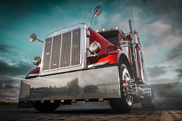 A classic red truck stands parked, showcasing its shiny chrome details against a cloudy, dramatic sunset sky.