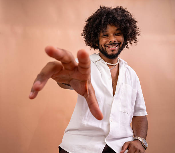 Young smiling adult man with curly hair reaching hand out towards the viewer