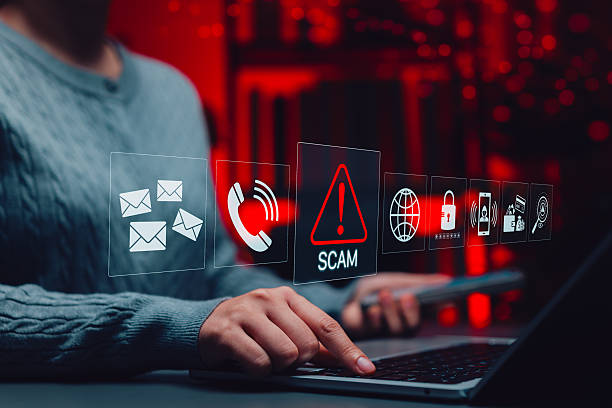 istock Online Scam Alert and Cybersecurity Threat Concept. Person using laptop and smart phone with red warning icons representing digital scams, email fraud, phishing, identity theft, cyber security threats 2242066104